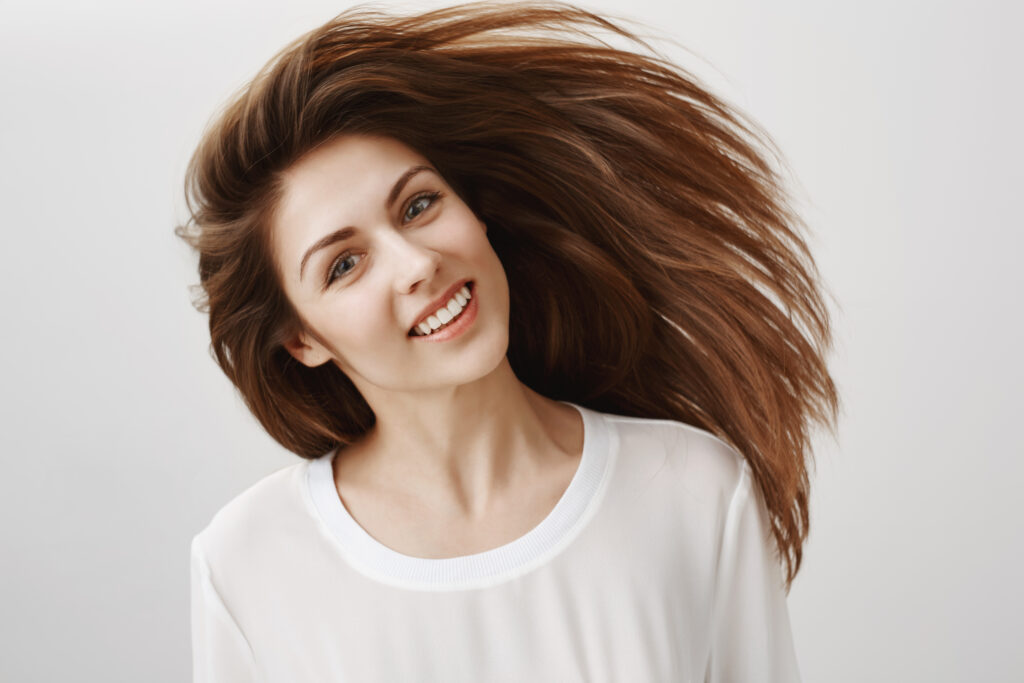 Healthy Hair Tips: Apne Baalon ko Sundar aur Mazboot Banane ke 5 Asardaar Tareeke happy people are beautiful. portrait of attractive young caucasian brunette waving head and smiling broadly, being satisfied with shampoo that straighten hair strands, standing over gray background